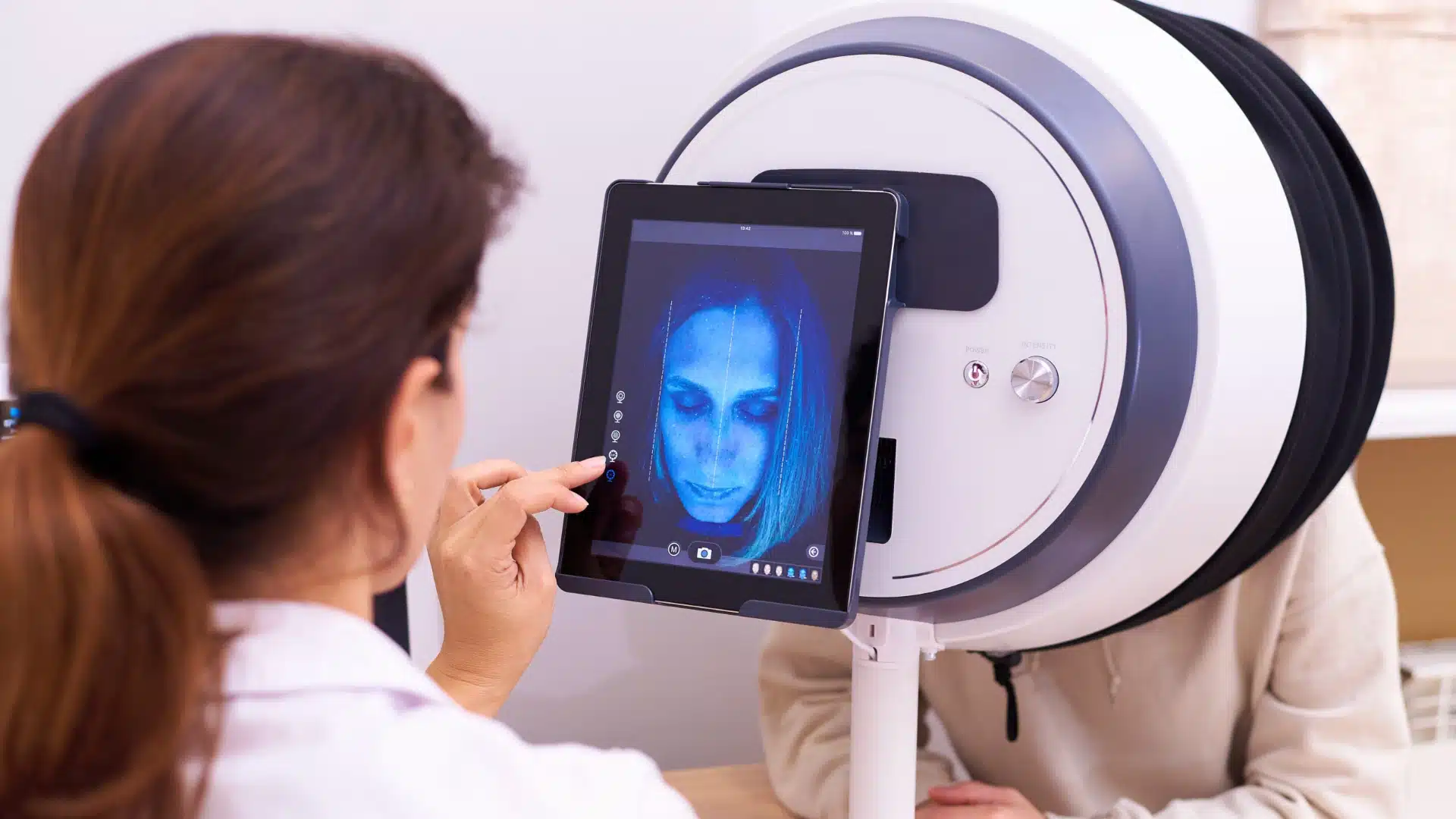 Dermatologist analyzing patient’s face with advanced skin scanner and digital imaging technology