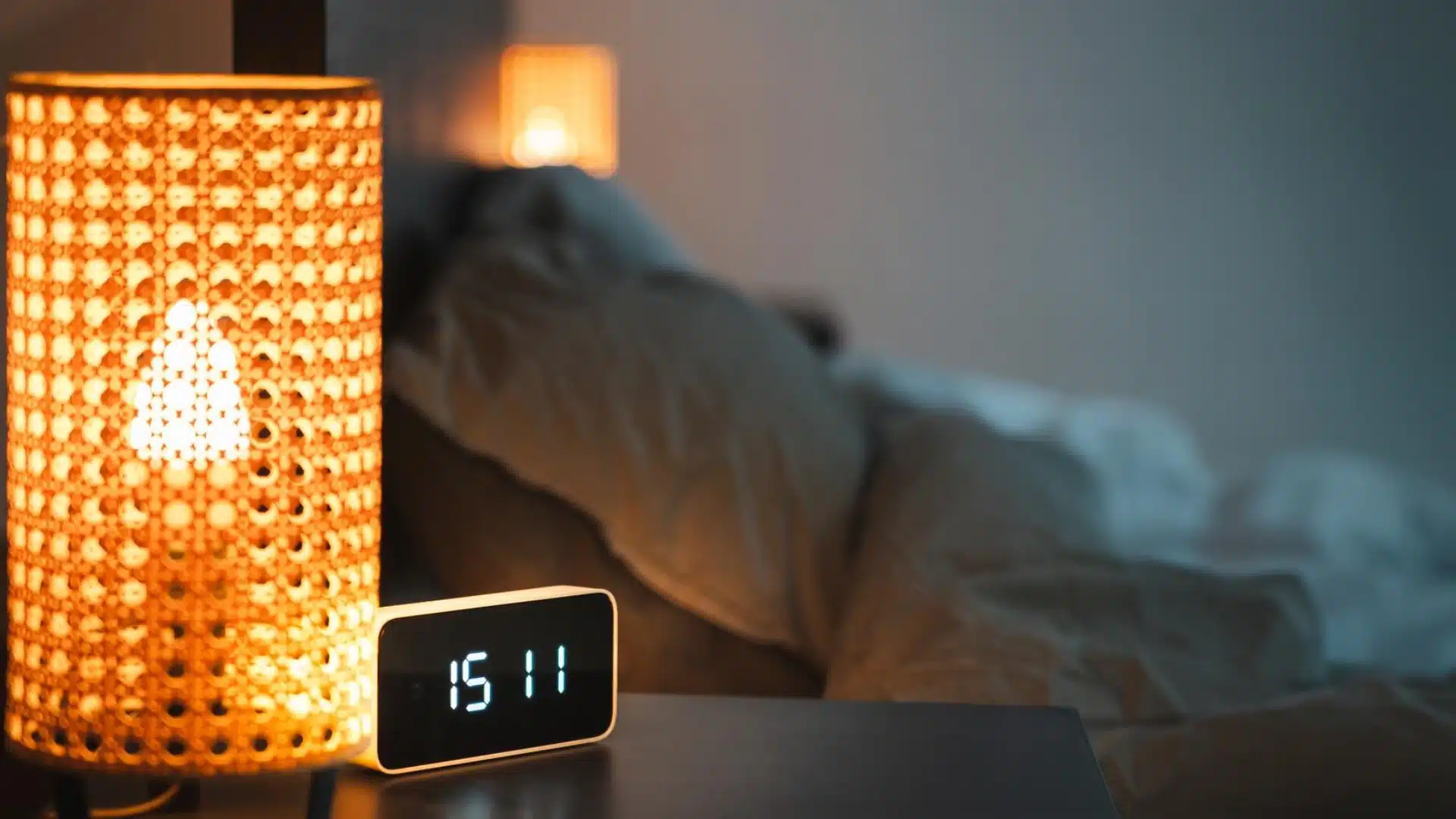 Digital alarm clock and bedside lamp in dim bedroom