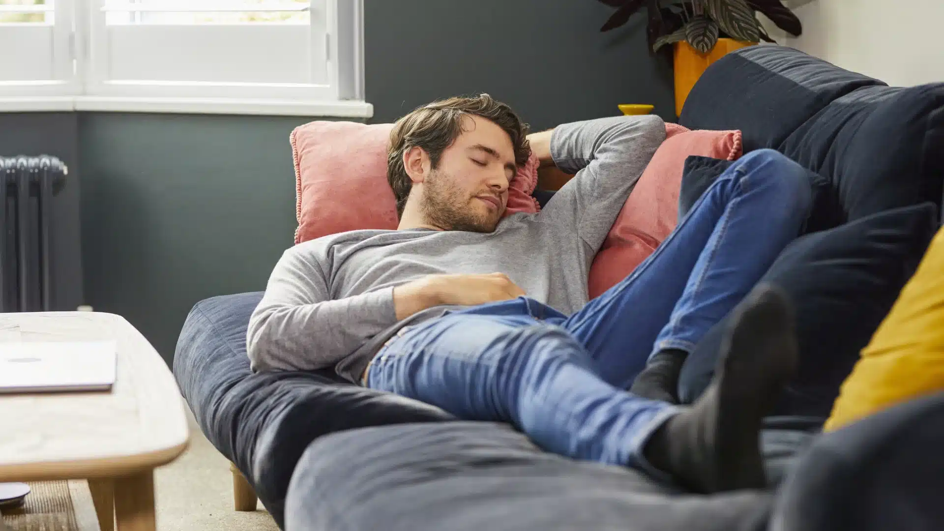 Young man sleeping on sofa during daytime, taking afternoon nap in casual clothes