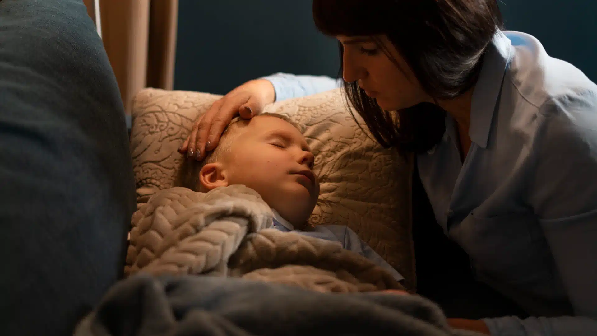 Mother gently comforting her sleeping child in bed with warm blanket at night