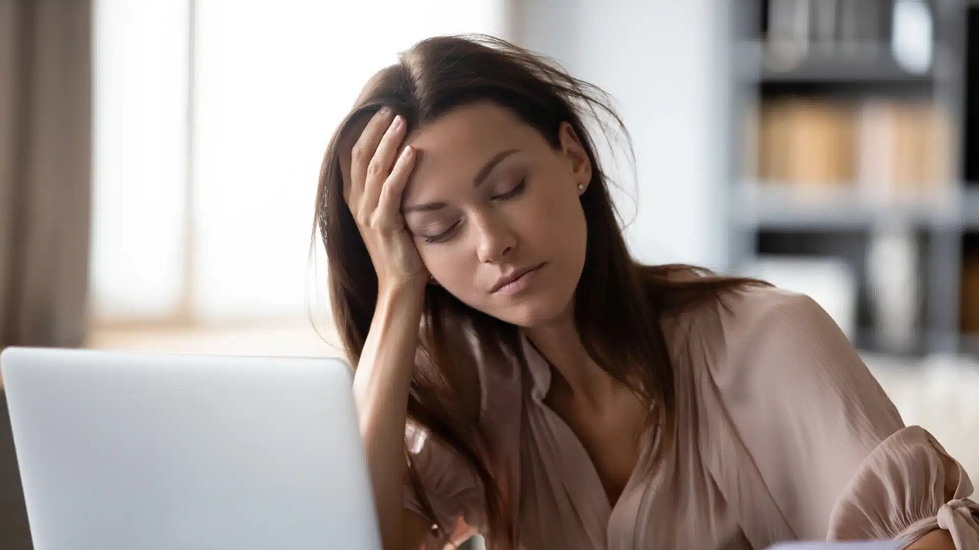 Tired woman struggling with fatigue and lack of sleep while working on laptop