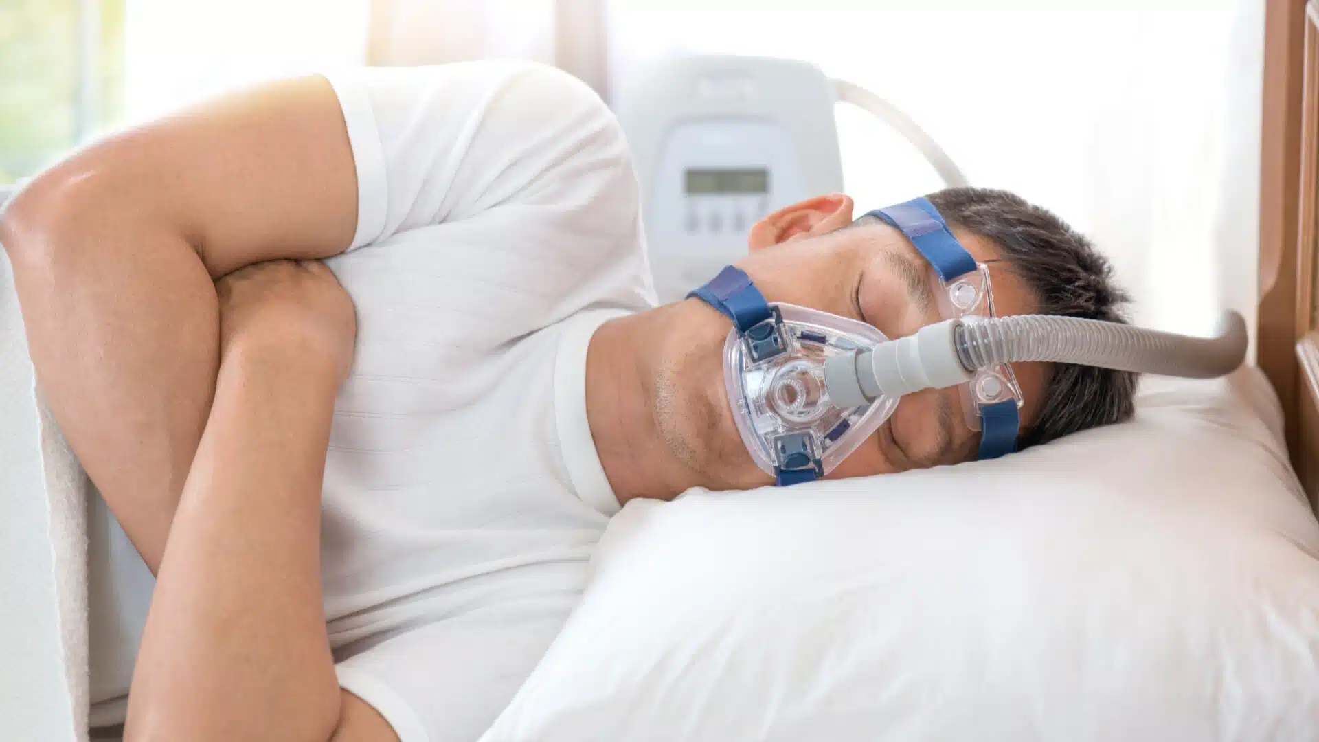 Middle-aged man wearing CPAP mask while sleeping on his side, using continuous positive airway pressure therapy machine to treat obstructive sleep apnea and improve nighttime breathing