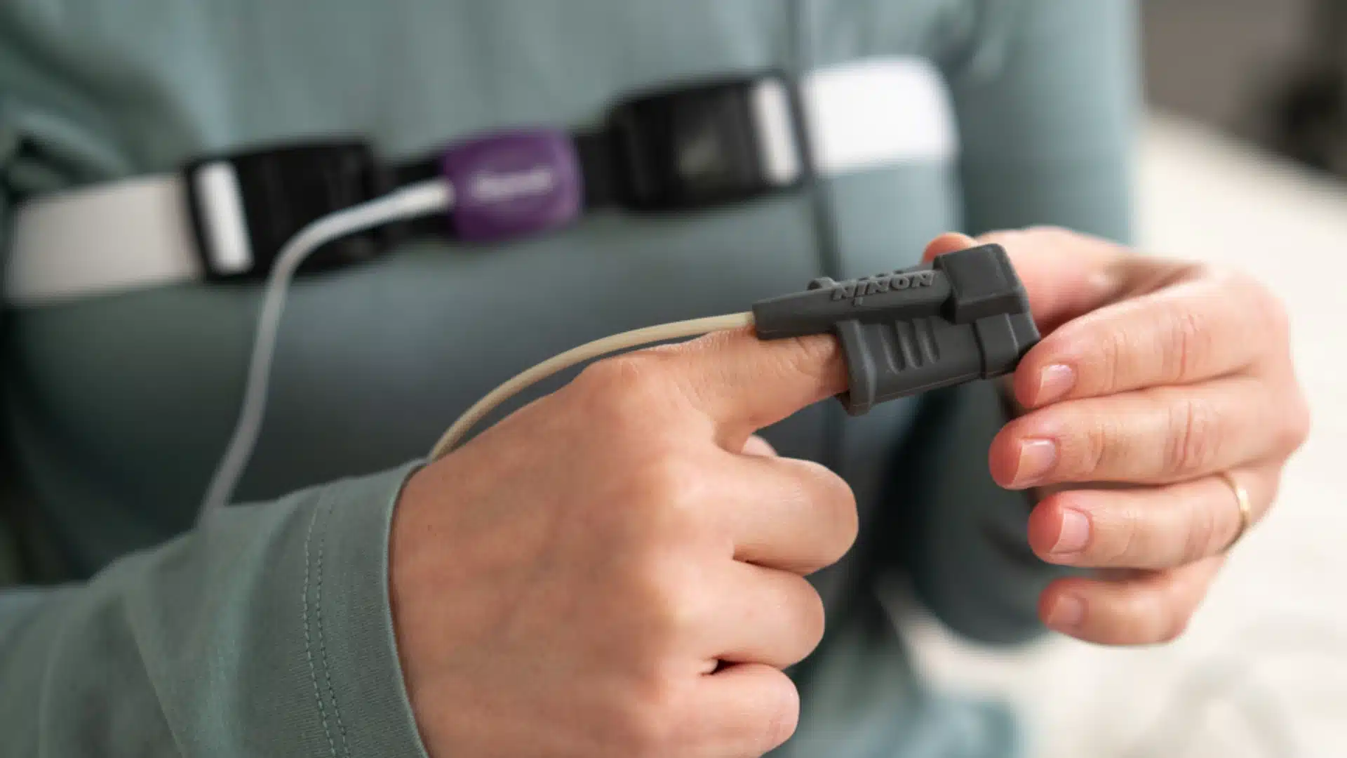 Close-up of person using home sleep apnea test device with finger pulse oximeter sensor and chest belt to monitor breathing during sleep study