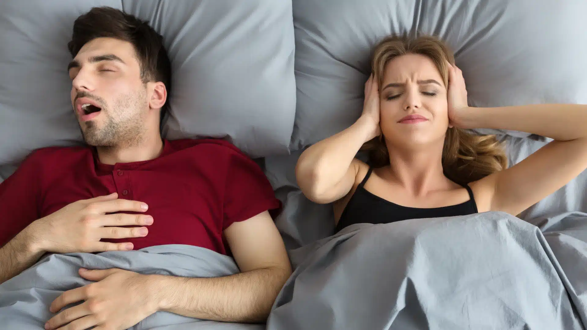 Woman covering ears in bed while man snores loudly beside her at night