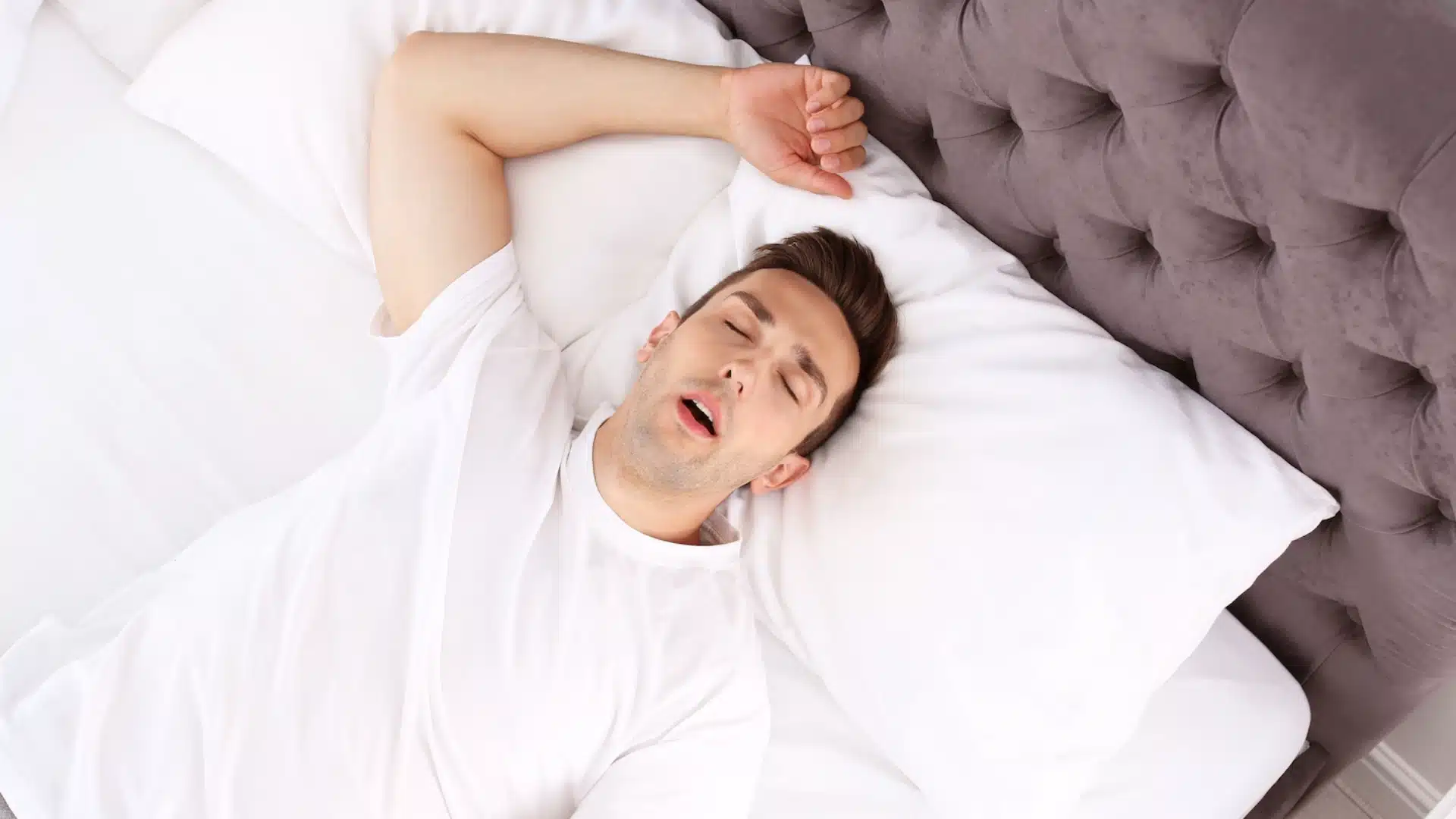 Young man sleeping on his back with mouth open, showing common symptom of sleep apnea and snoring, potential breathing issues during sleep