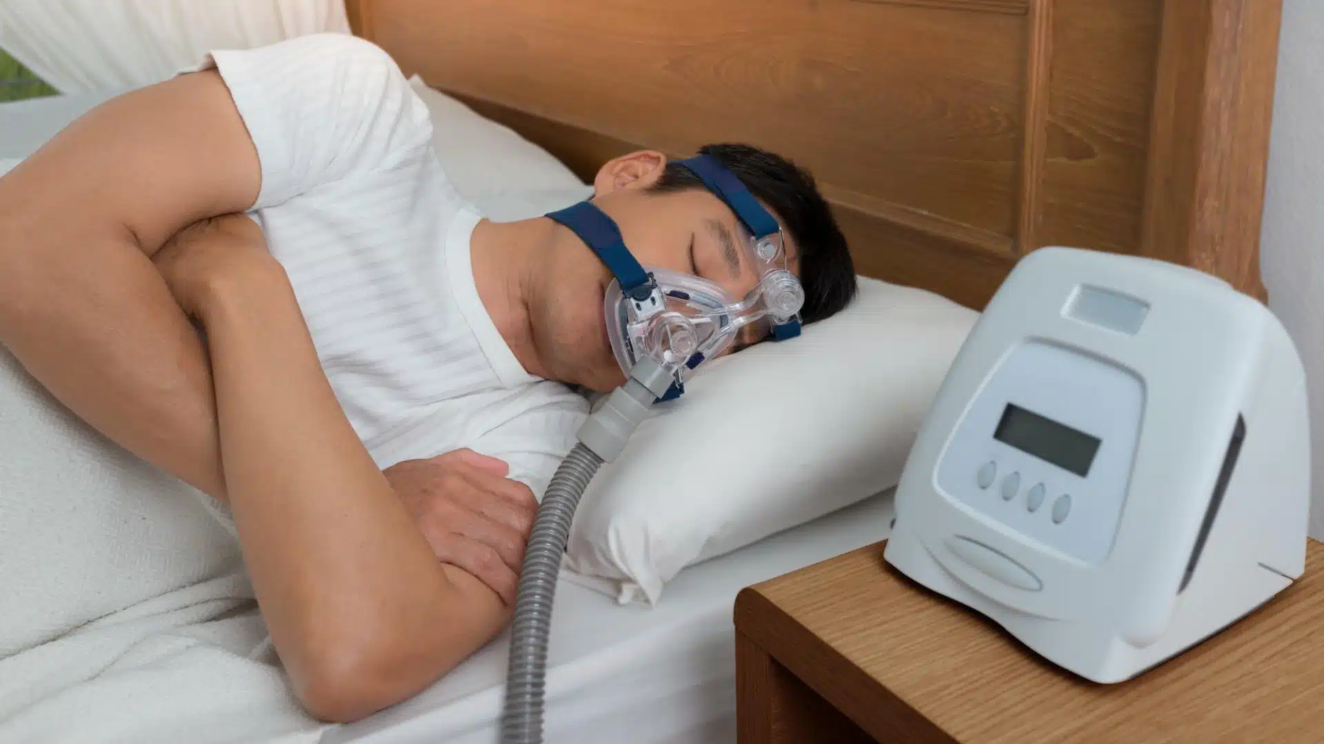 Man sleeping with CPAP mask and machine on bedside table