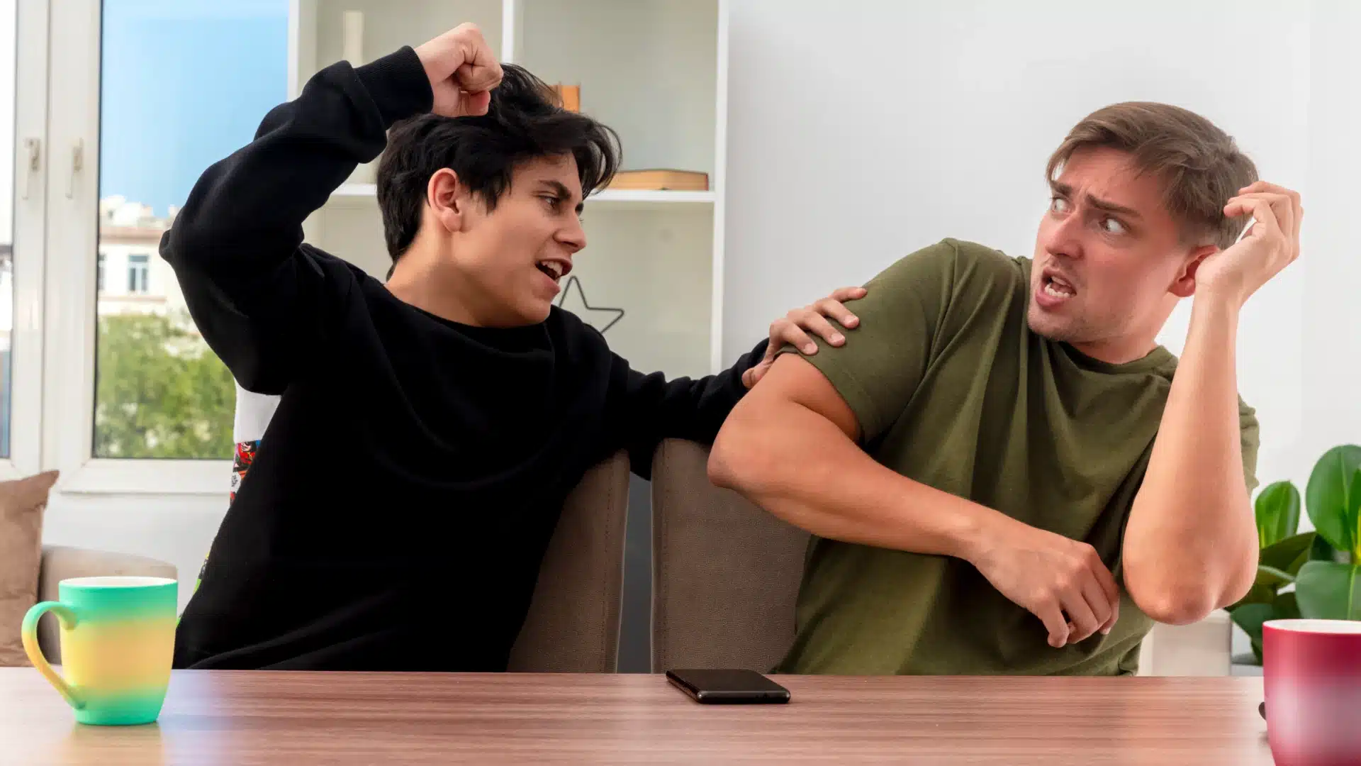 Two young men arguing at home with one raising fist and the other reacting defensively