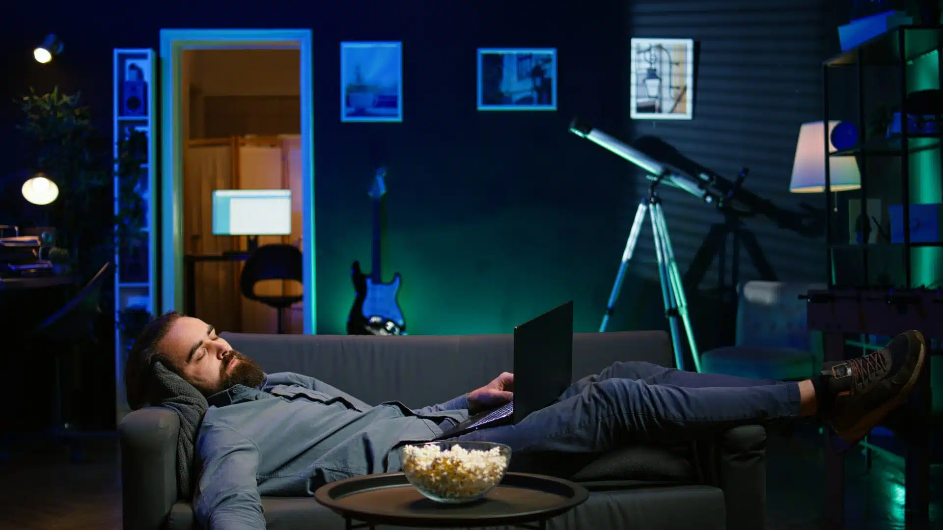 Man falling asleep on couch with laptop after working late at night in living room