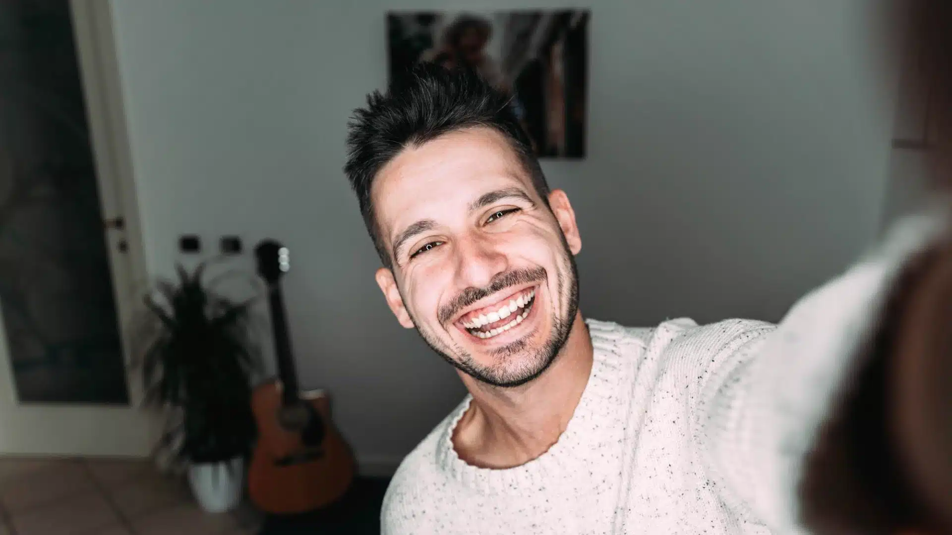 Smiling young man taking a cheerful selfie at home in casual sweater