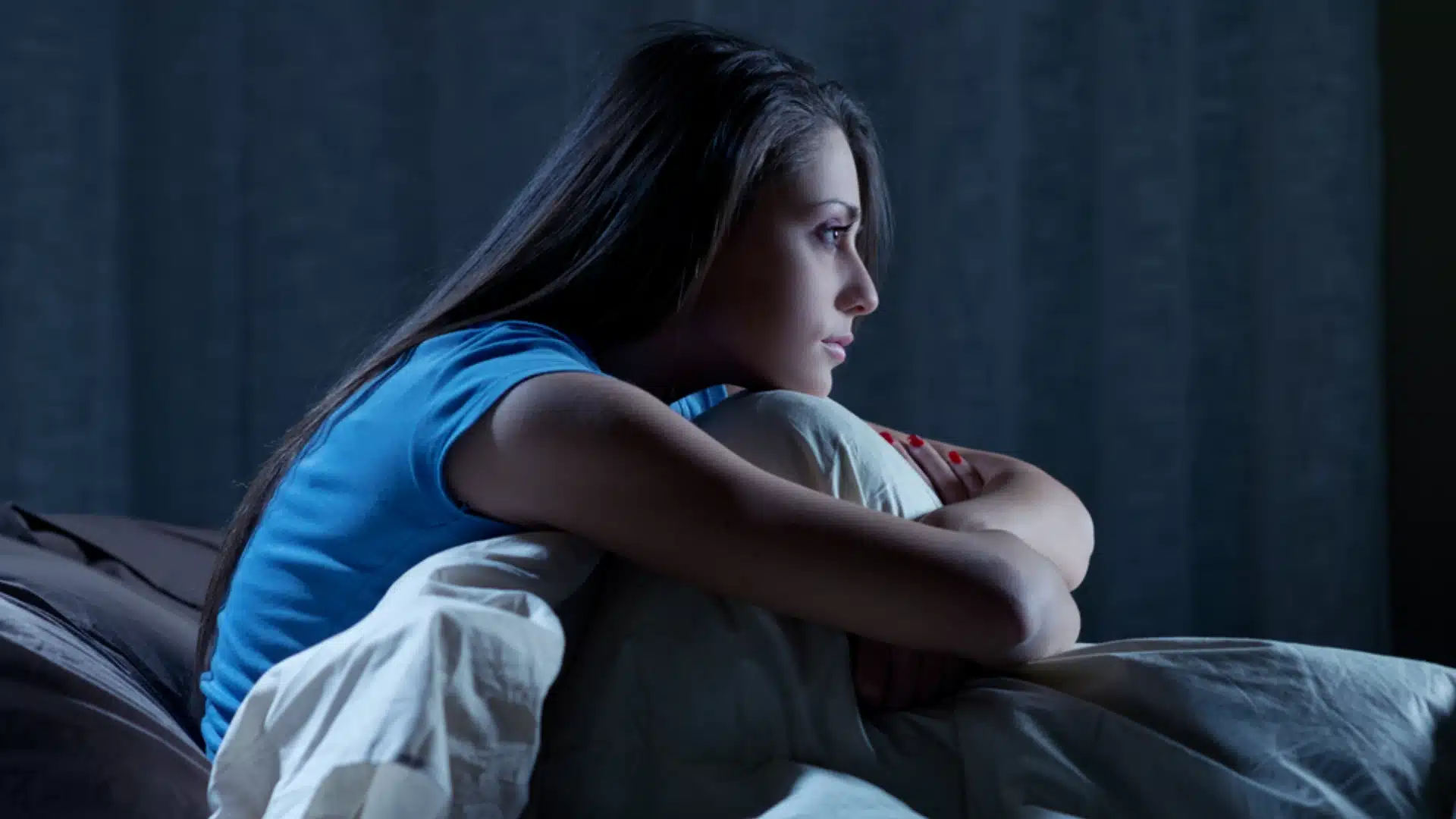 Woman struggling with insomnia sitting awake in bed at night