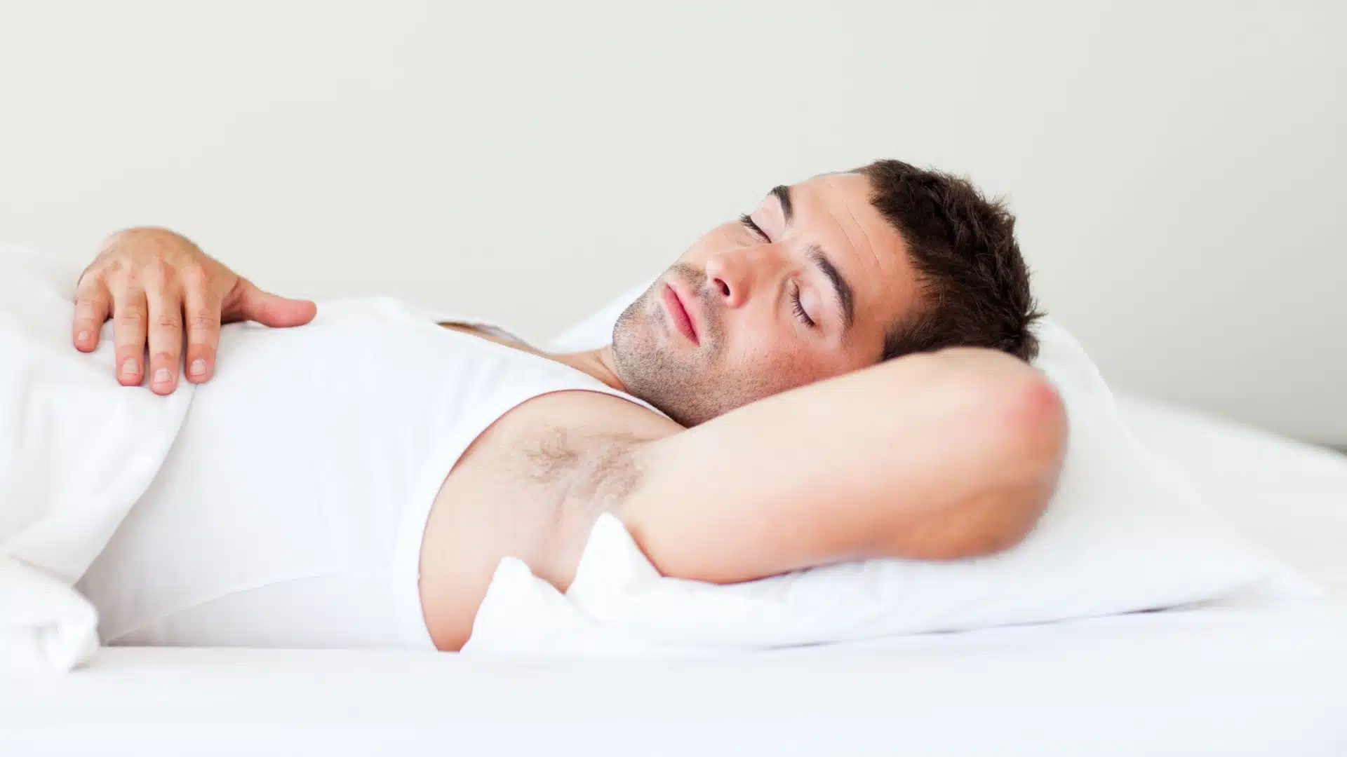 Young man sleeping peacefully on white bed in comfortable position with hand on chest