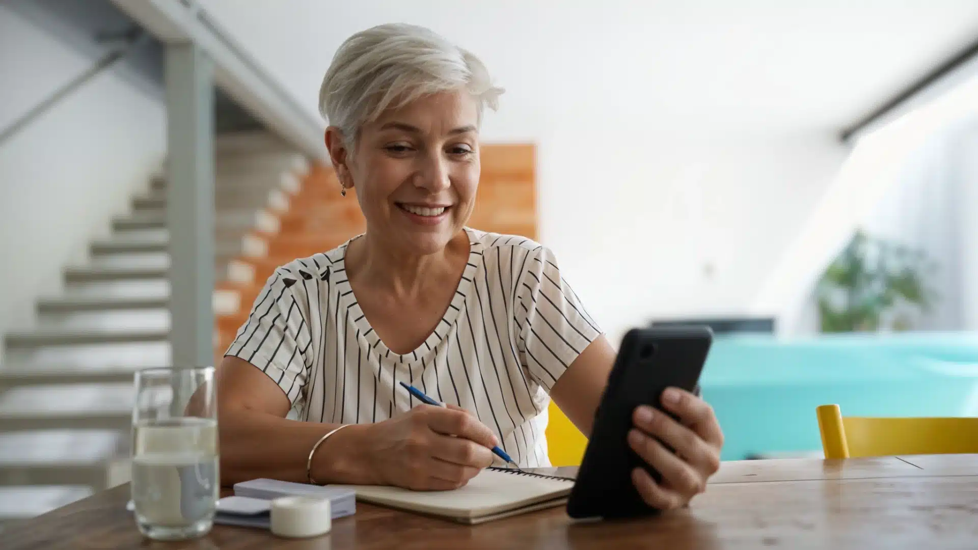 Smiling senior woman taking notes while having a video call on smartphone at home
