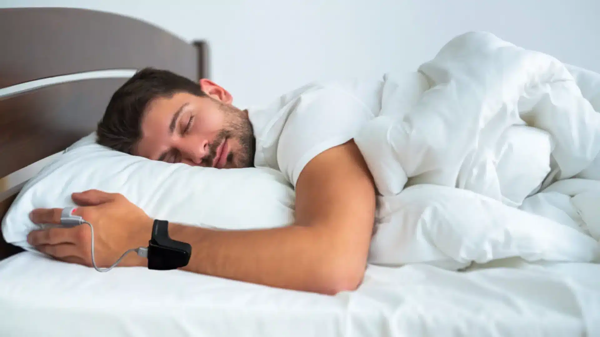 Man sleeping in bed while wearing a pulse oximeter on wrist and finger for overnight oxygen monitoring